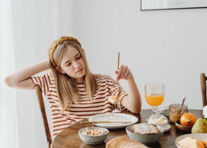 Teen girl in striped shirt at breakfast table with fruits, bread, and juice. Casual morning setting.