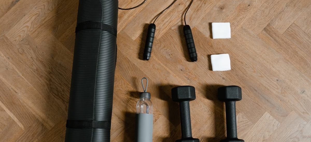 Flat lay of exercise essentials including dumbbells, yoga mat, and water bottle on wooden floor.