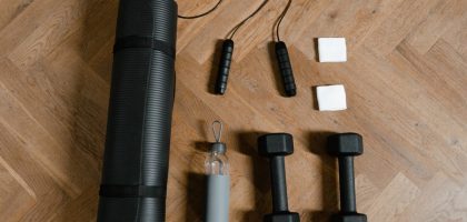 Flat lay of exercise essentials including dumbbells, yoga mat, and water bottle on wooden floor.