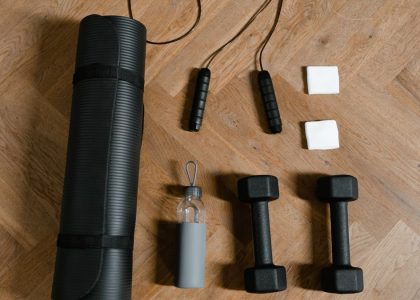 Flat lay of exercise essentials including dumbbells, yoga mat, and water bottle on wooden floor.